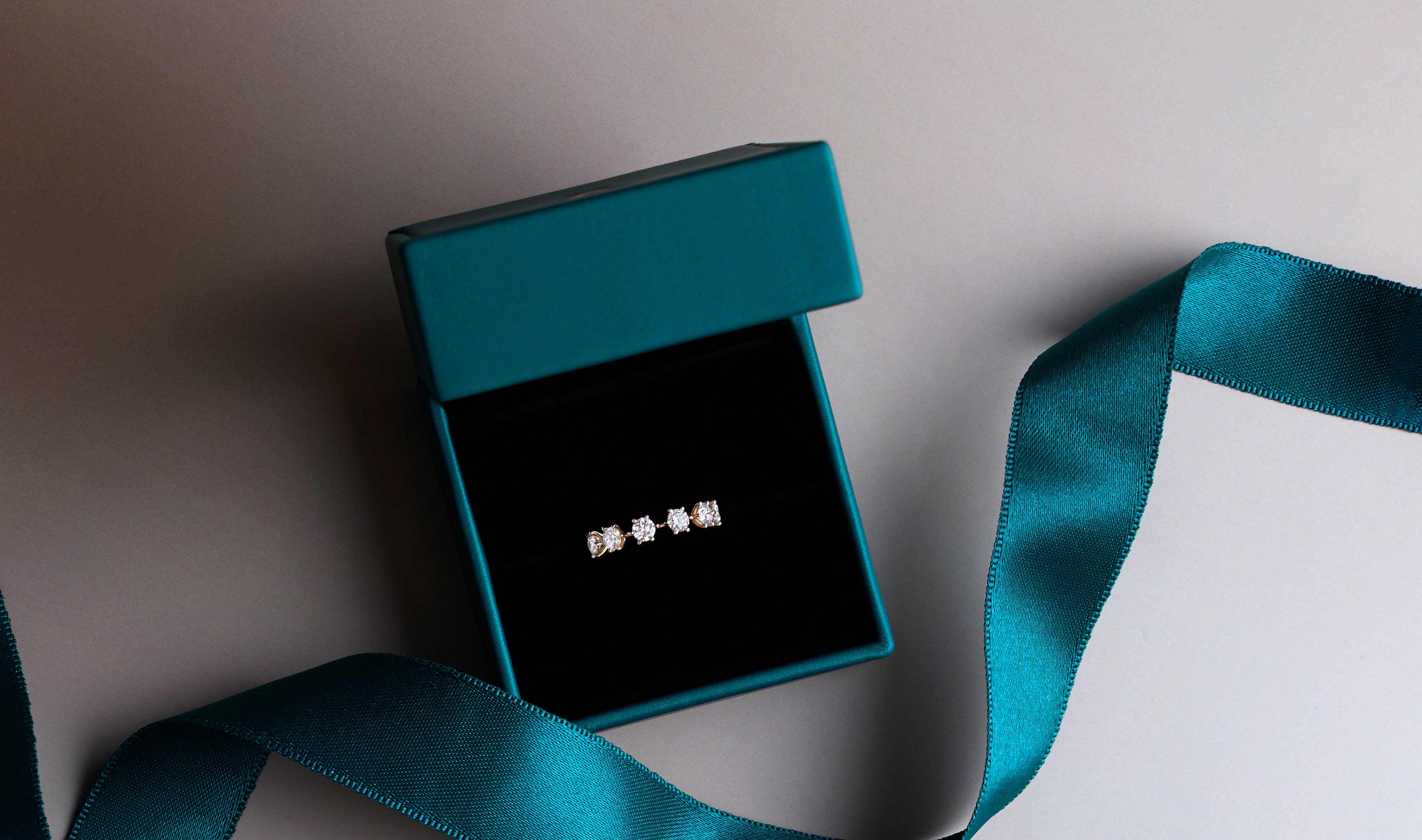 Elegant five-stone diamond ring displayed in a luxurious teal gift box, adorned with a matching teal ribbon. Ideal diamond jewelry for engagements, anniversaries, or special gifts.
