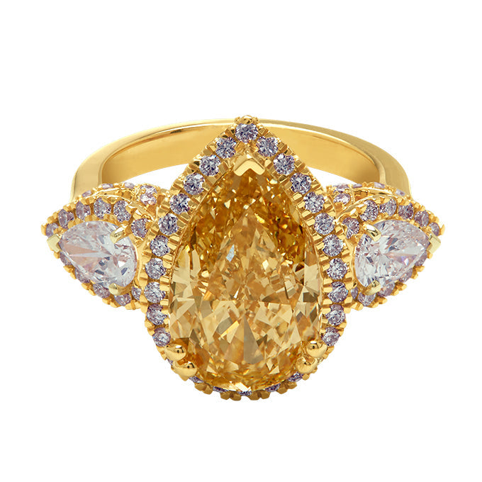 Aukera Champagne Heartline Pear Ring, a luxurious yellow gold three-stone diamond ring. Features a stunning pear-cut champagne diamond at its center, flanked by two clear pear-cut diamonds, all accented with dazzling diamond halos.