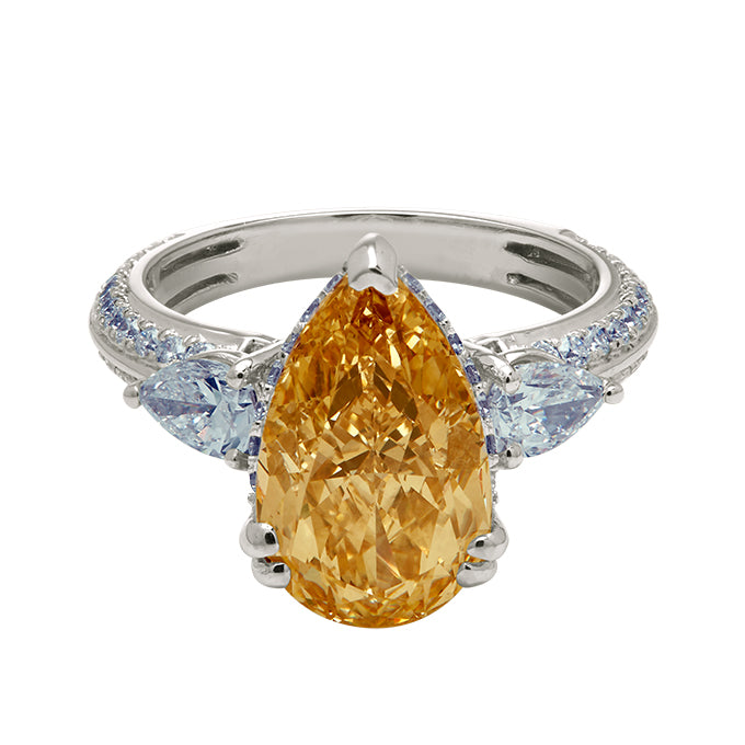 The Champagne Flame Pear Ring, a yellow pear-shaped diamond engagement ring with pear side diamonds and a diamond-encrusted white gold band. Luxury diamond jewelry.