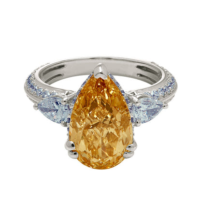 The Champagne Flame Pear Ring, a yellow pear-shaped diamond engagement ring with pear side diamonds and a diamond-encrusted white gold band. Luxury diamond jewelry.