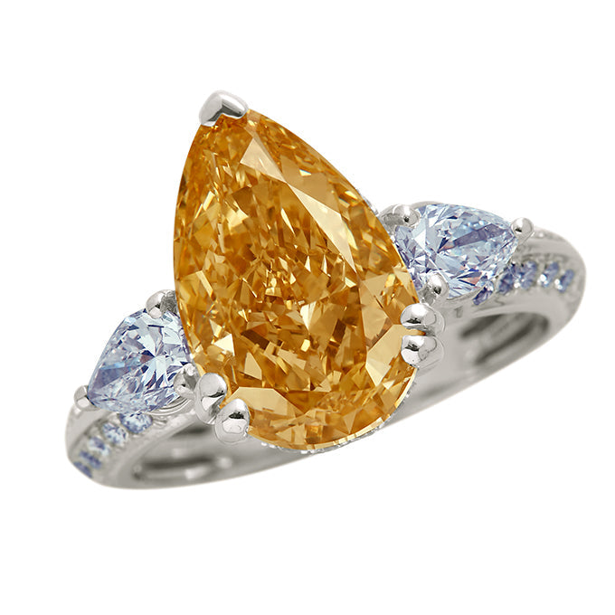 The Champagne Flame Pear Ring: A luxurious pear-shaped champagne diamond ring with blue diamond accents on a pavé diamond band. Ideal as an engagement ring or fine jewelry piece.