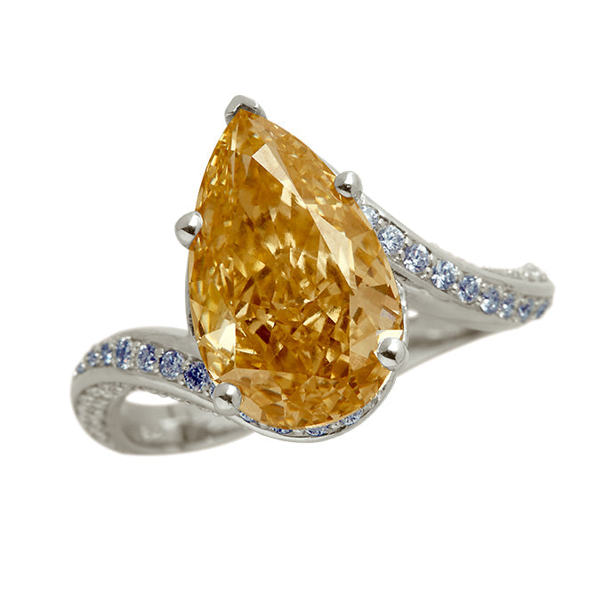 The Champagne Wave Pear Ring: A stunning pear-shaped champagne diamond ring set in a white gold wave band, accented with sparkling blue diamonds. Ideal for luxury diamond jewelry and engagement rings.