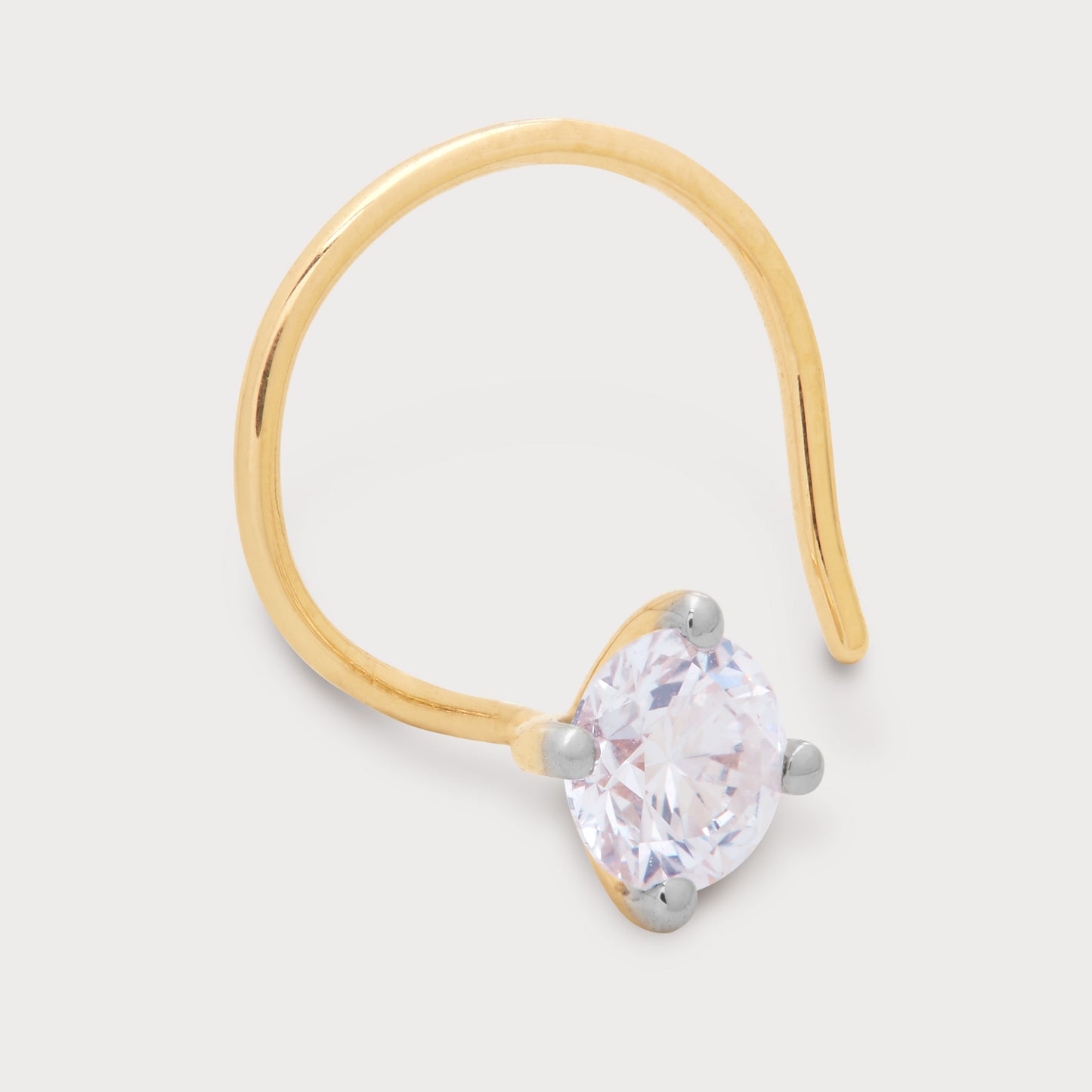 The Radiant Solitary Nose Pin - a close-up of a sparkling round brilliant diamond set in a golden curved nose pin with white gold prongs, against a plain background. This elegant diamond nose pin is perfect for those seeking radiant diamond jewellery.