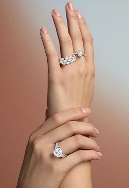 Hand wearing two diamond rings on a gradient background