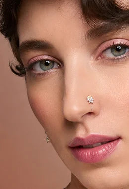 Close-up of a model wearing a small, clear, star-shaped stud nose ring against a warm beige background.